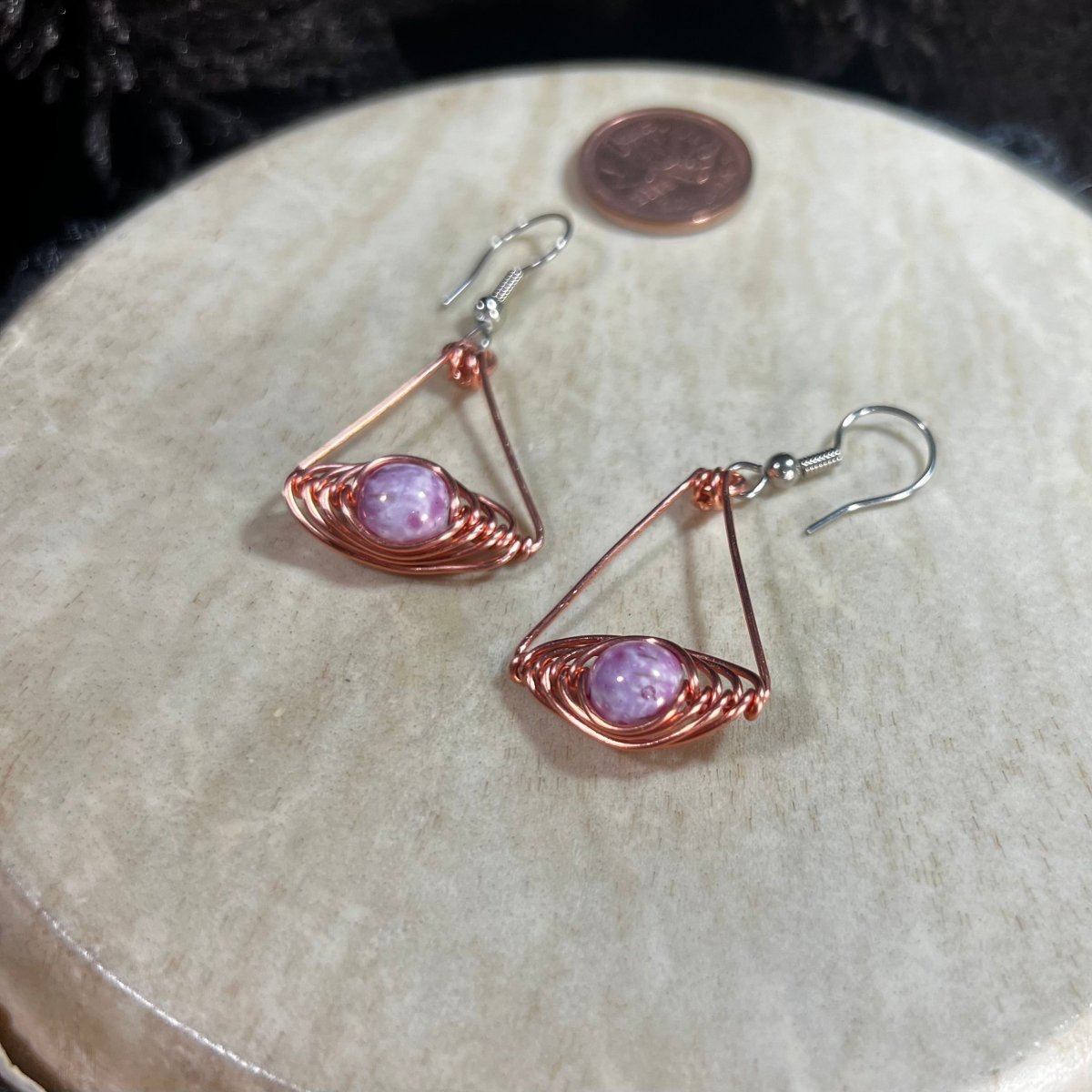 Copper wire earrings with pink/purple stones on a beige surface