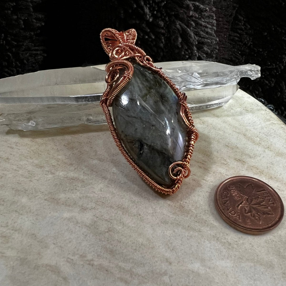 Labradorite pendant with  copper wire wrapping on a neutral surface with a CAnadian penny for scale.
