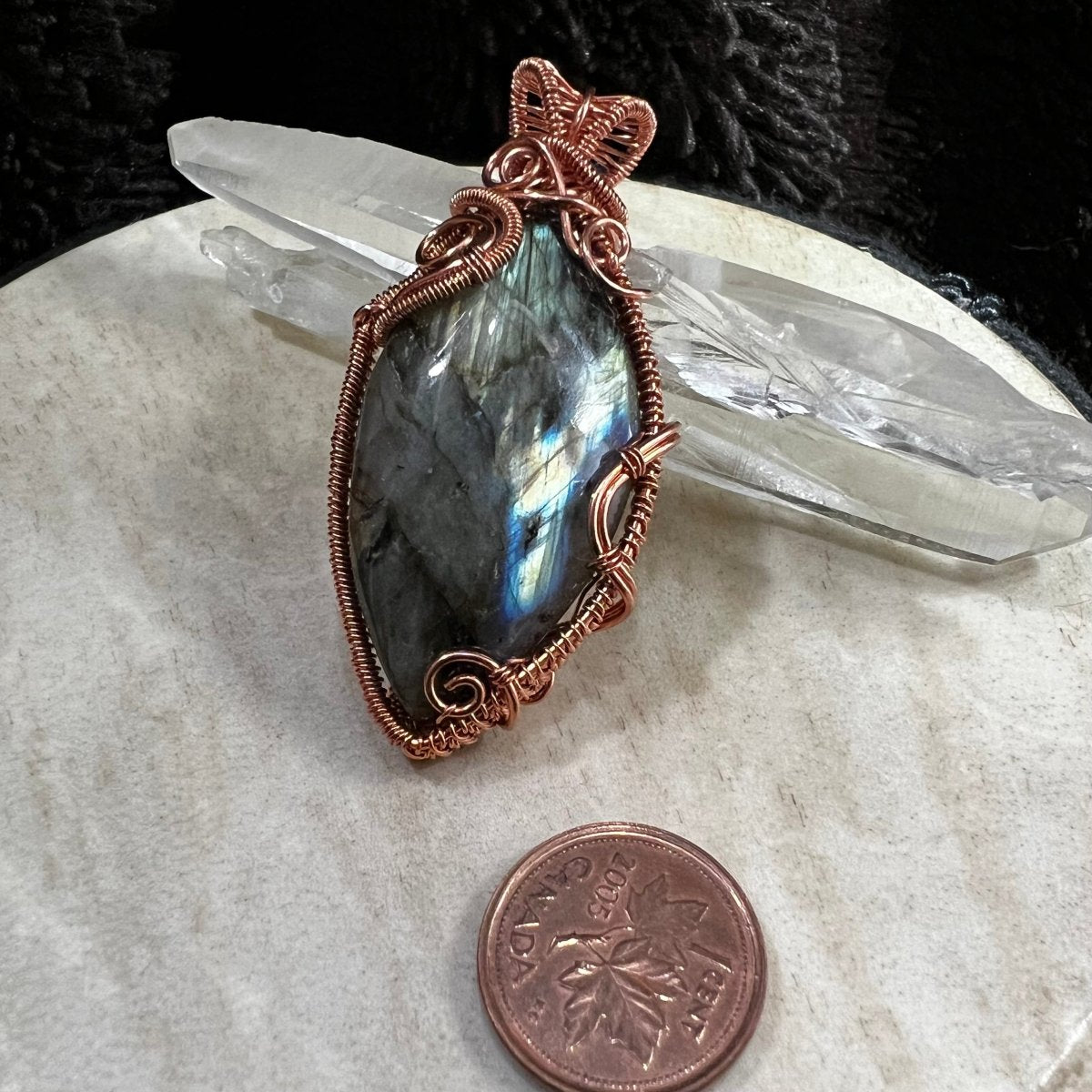 Labradorite stone pendant with copper wire wrapping on a white surface with a Canadian penny for scale.
