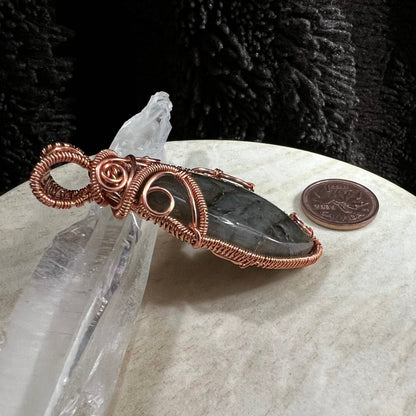Side view of a labradorite pendant wrapped in reclaimed copper, handmade protection crystal necklace with dark stone on neutral background