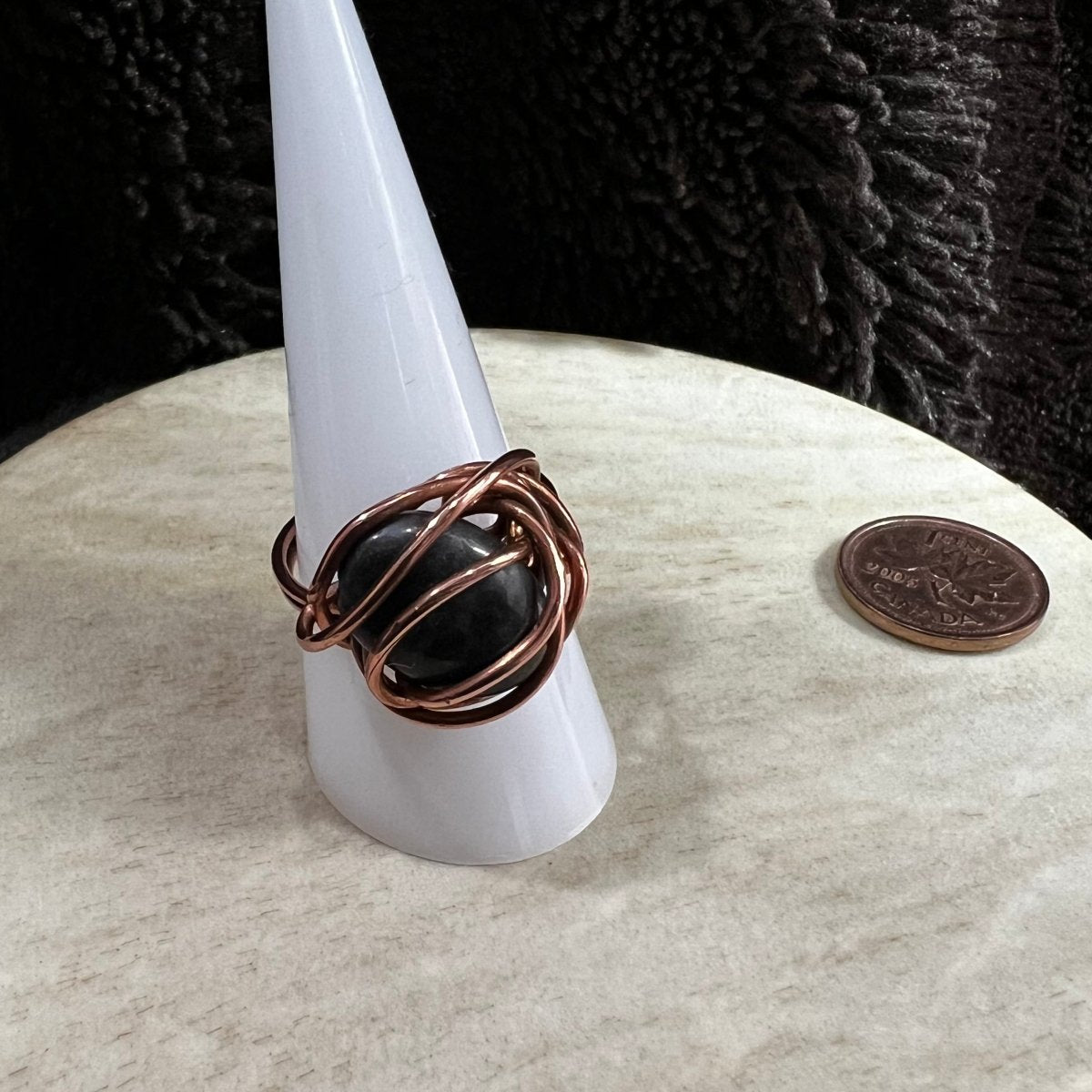 Copper wire-wrapped ring on a white stand with a black background