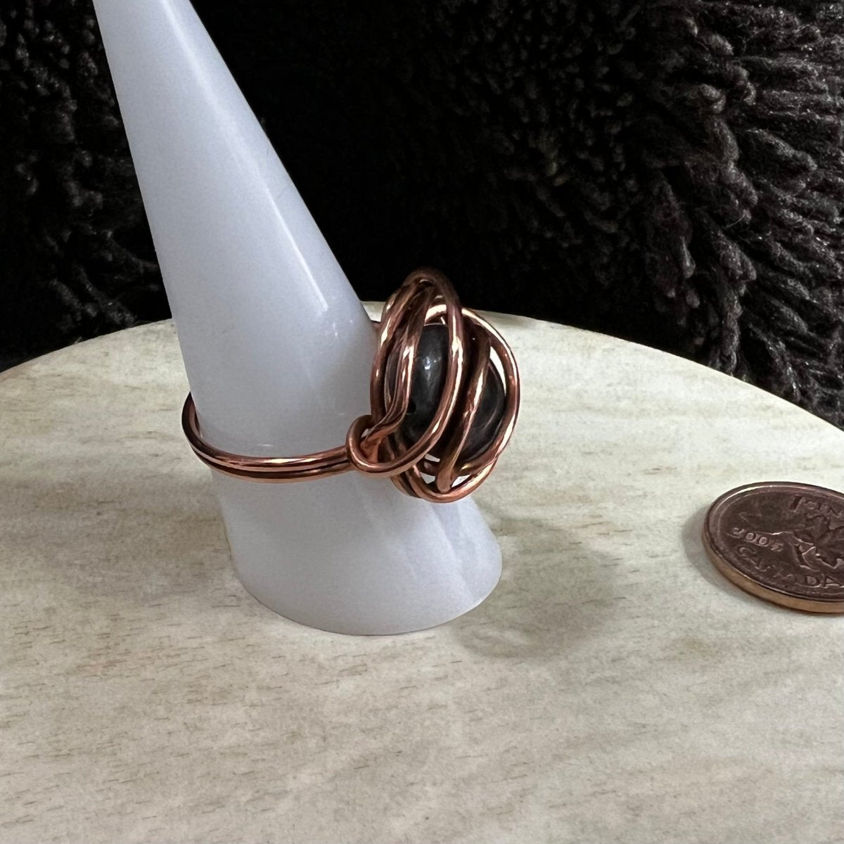 Copper ring with black larvikite stone on a white stand, next to a penny for scale.