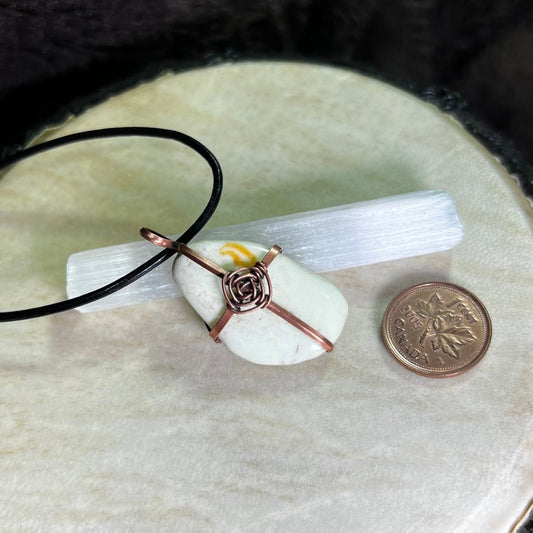 Necklace with a pendant on a white stone, next to a penny for scale, on a textured surface.