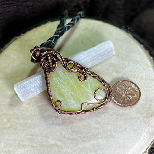 Copper wire-wrapped pendant with selenite crystal on a white surface next to a penny for scale