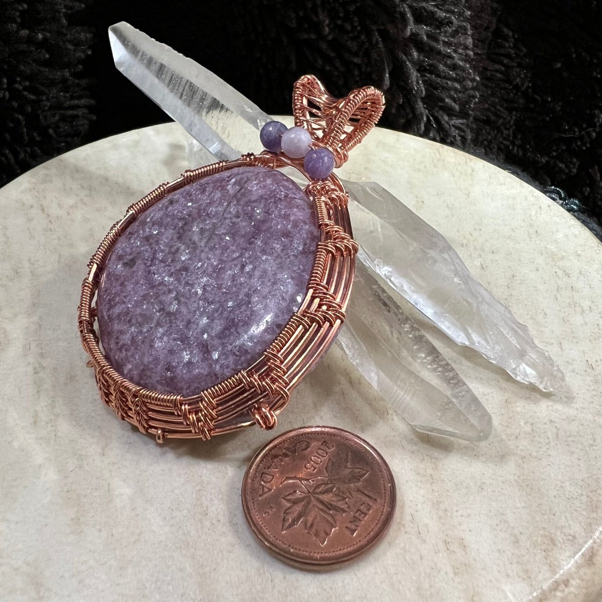 Purple lepidolite stone in a copper wire frame with clear crystals on a beige surface