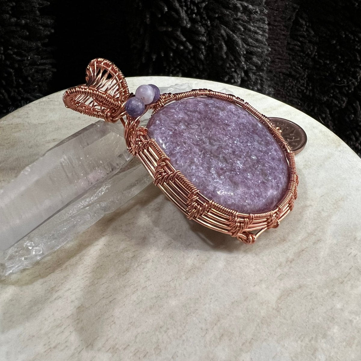 Purple lepidolite stone pendant with copper wire wrapping on a beige surface