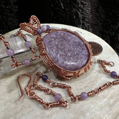 Jewelry set with a purple lepidolite stone pendant and matching bracelets on a beige surface.