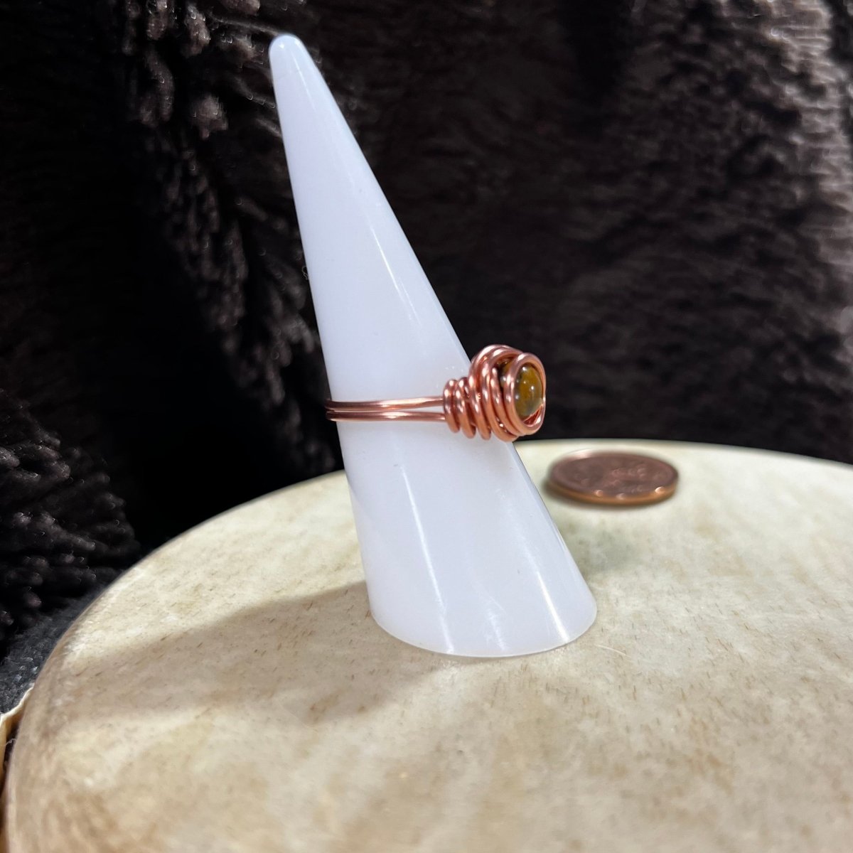 Nest ring with a yellow Mookaite gemstone on a white cone against a textured dark background