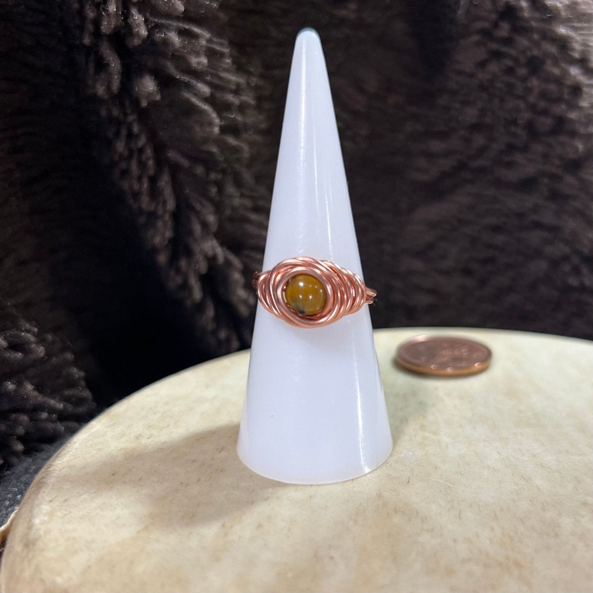 Nest ring with a yellow Mookaite gemstone on a white cone against a textured dark background