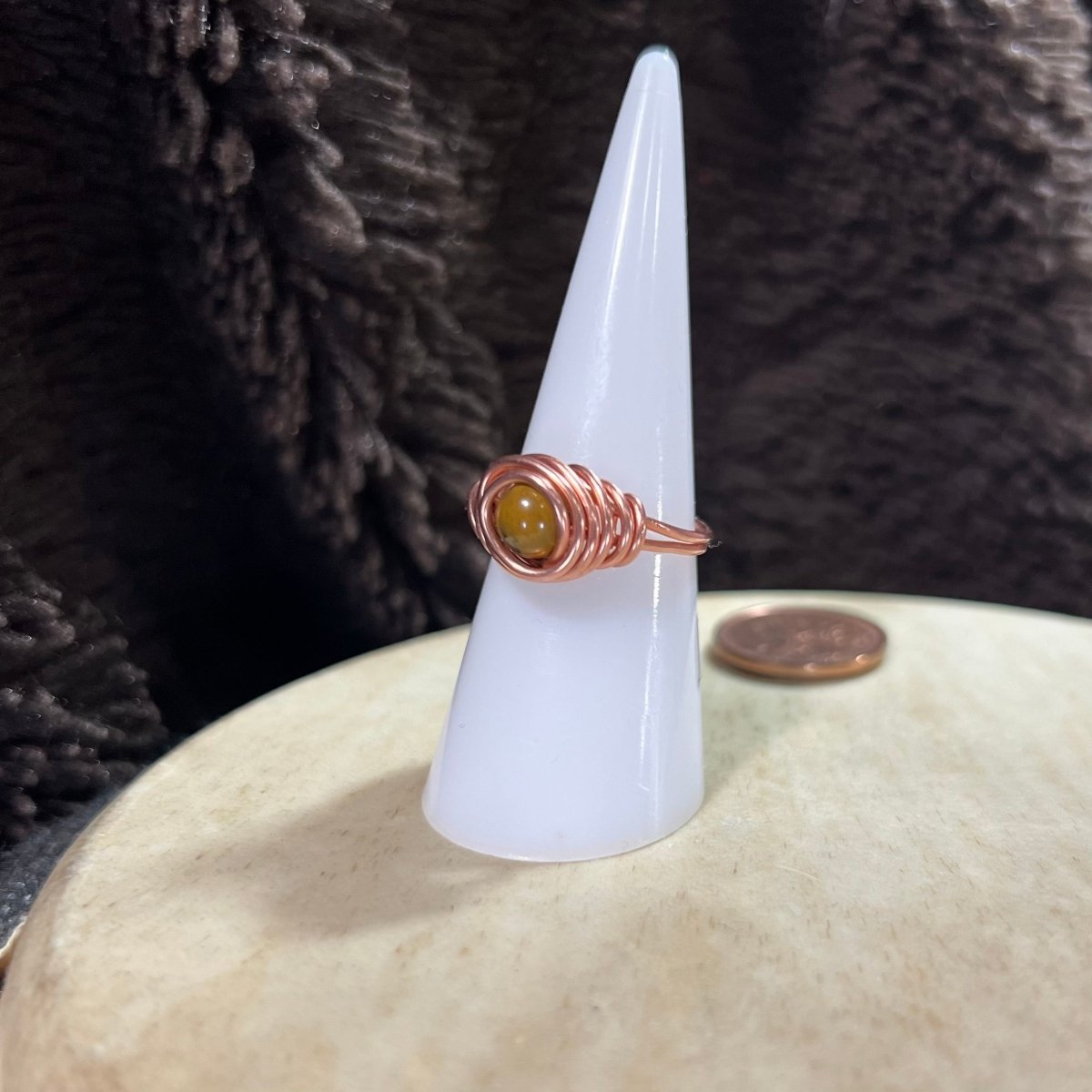 Nest ring with a yellow Mookaite gemstone on a white cone against a textured dark background