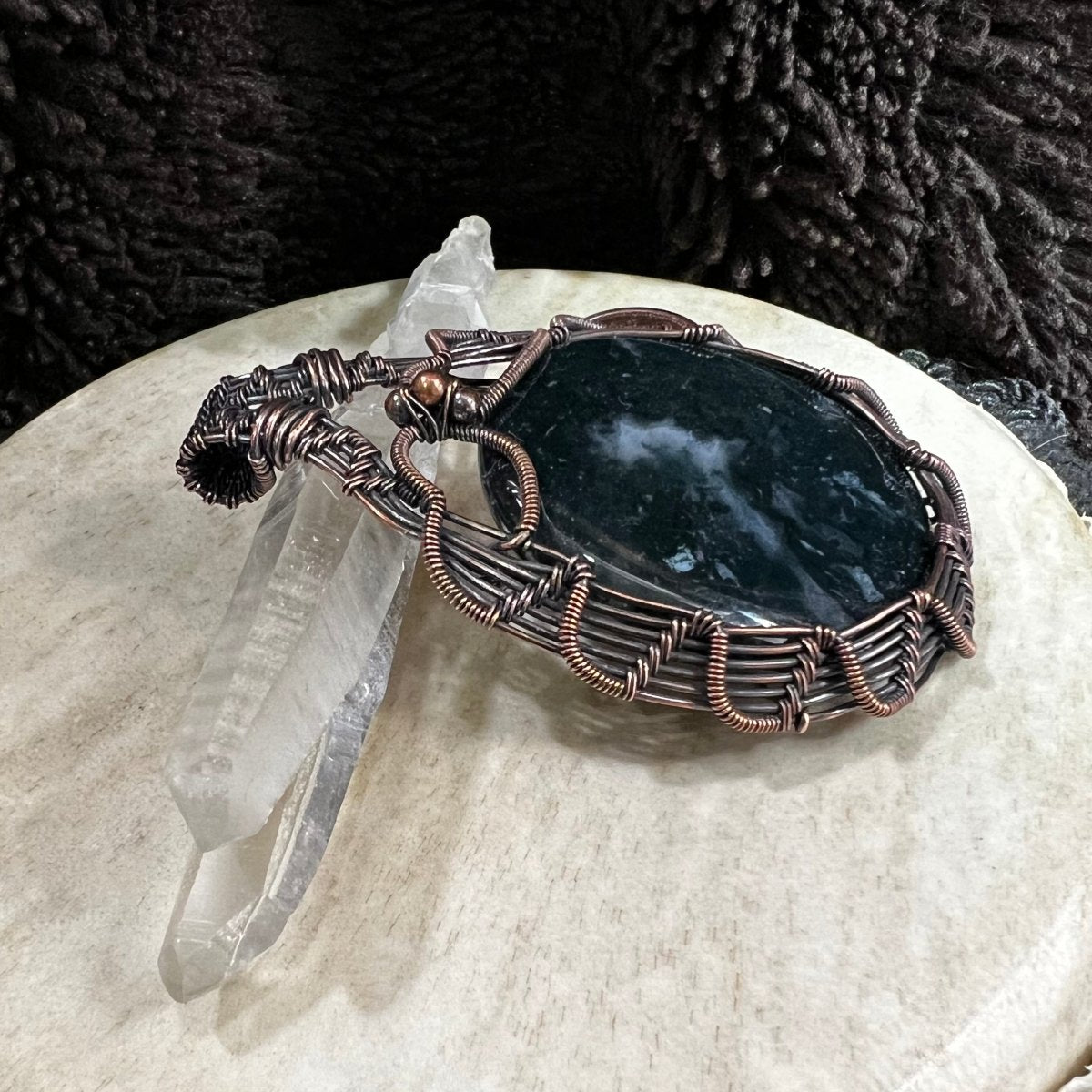 Side view of copper-wrapped moss agate pendant highlighting layered wirework
