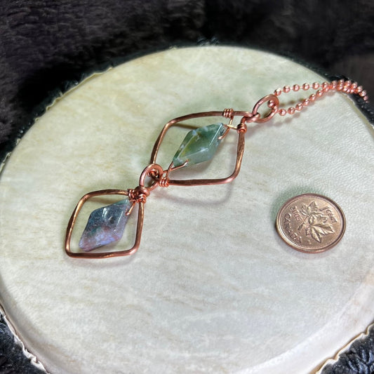 Hand made diamond motif copper necklace with moss agate gemstones on a white surface with a penny for scale.