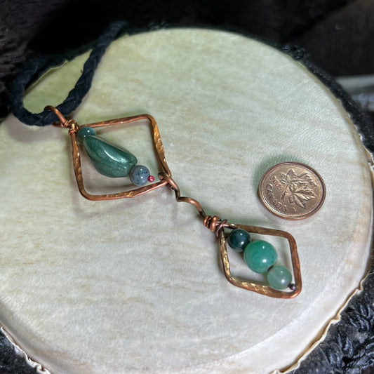Diamond Motif necklace with moss agate  stones and copper accents on a round  beige surface.