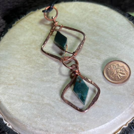 Copper 2 piece diamond-shaped pendant with moss agate gemstones on a beige surface with a penny for scale.