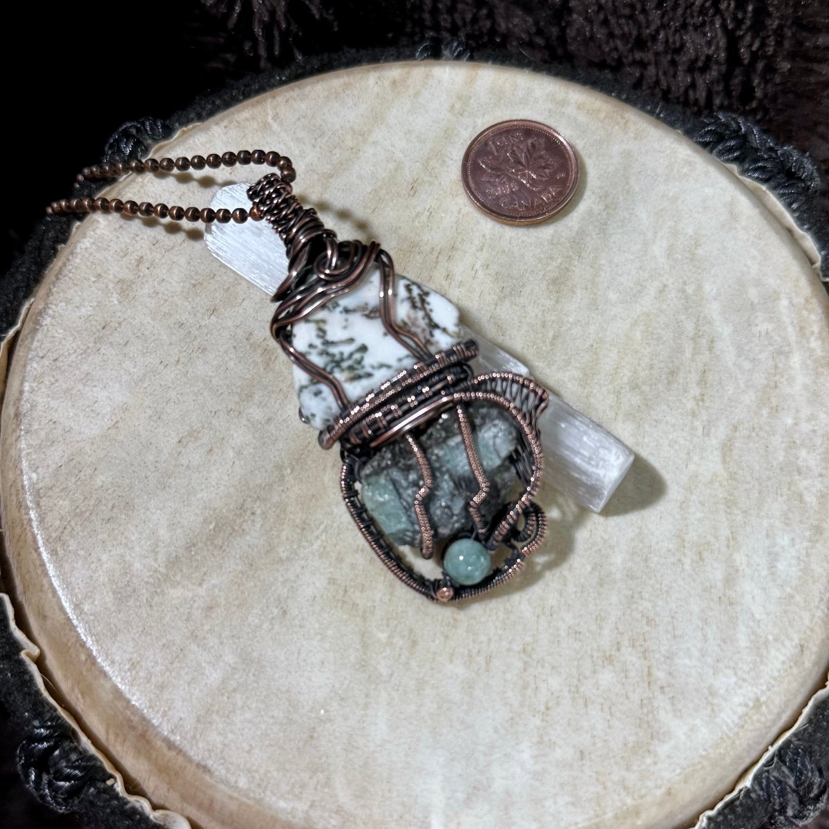 Angled view of the Moss Agate and Emerald Growthkeeper necklace showing its handwoven patinated copper setting and 20-inch ball chain.