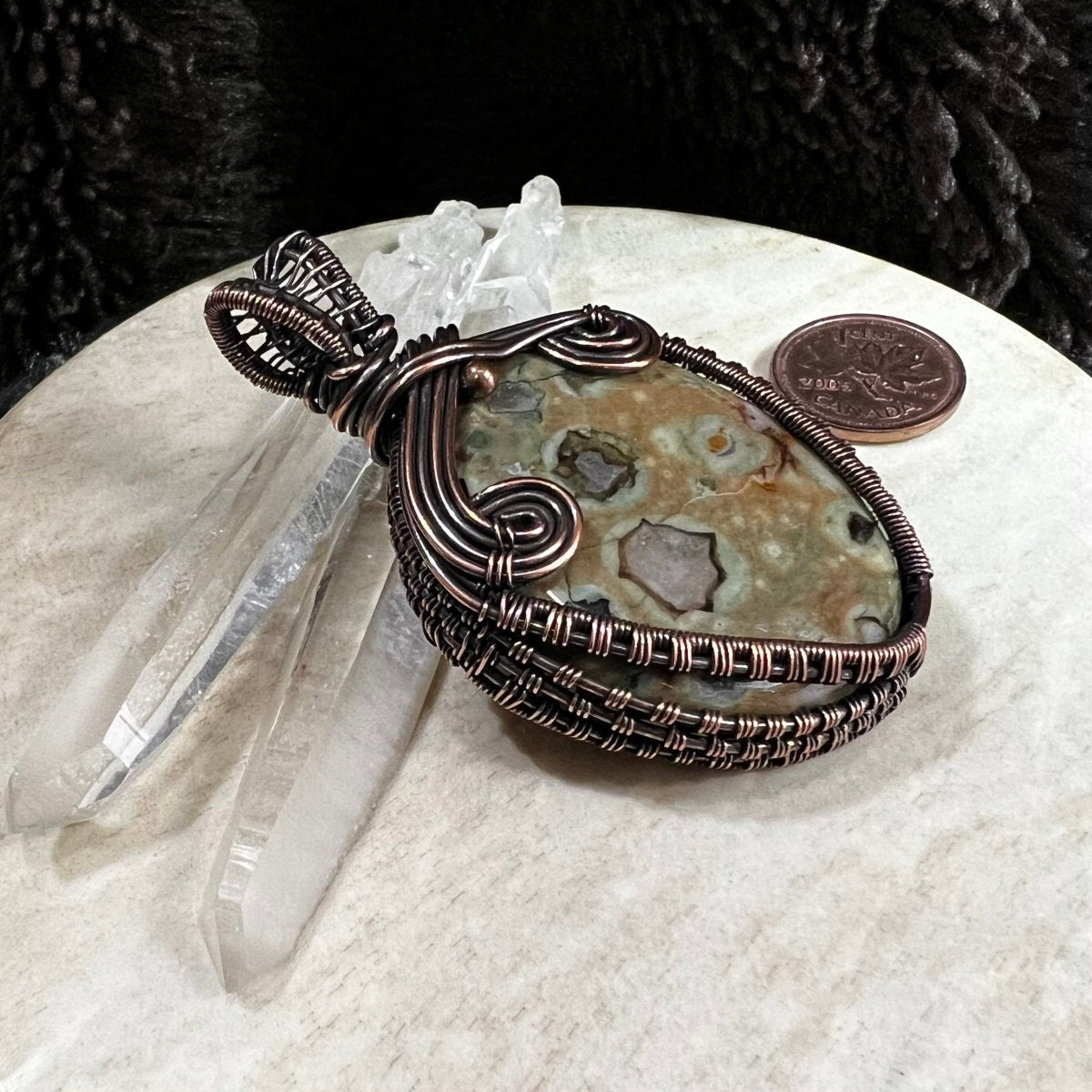 Ocean jasper pendant displayed with quartz crystals and Canadian penny for scale and contrast