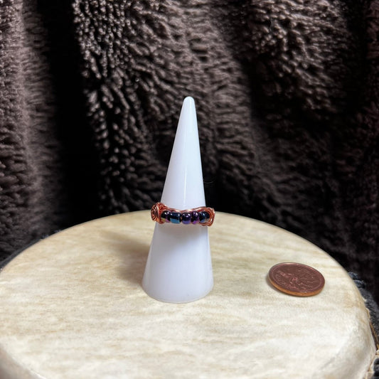 Ring on a white cone with a coin for scale against a textured brown background