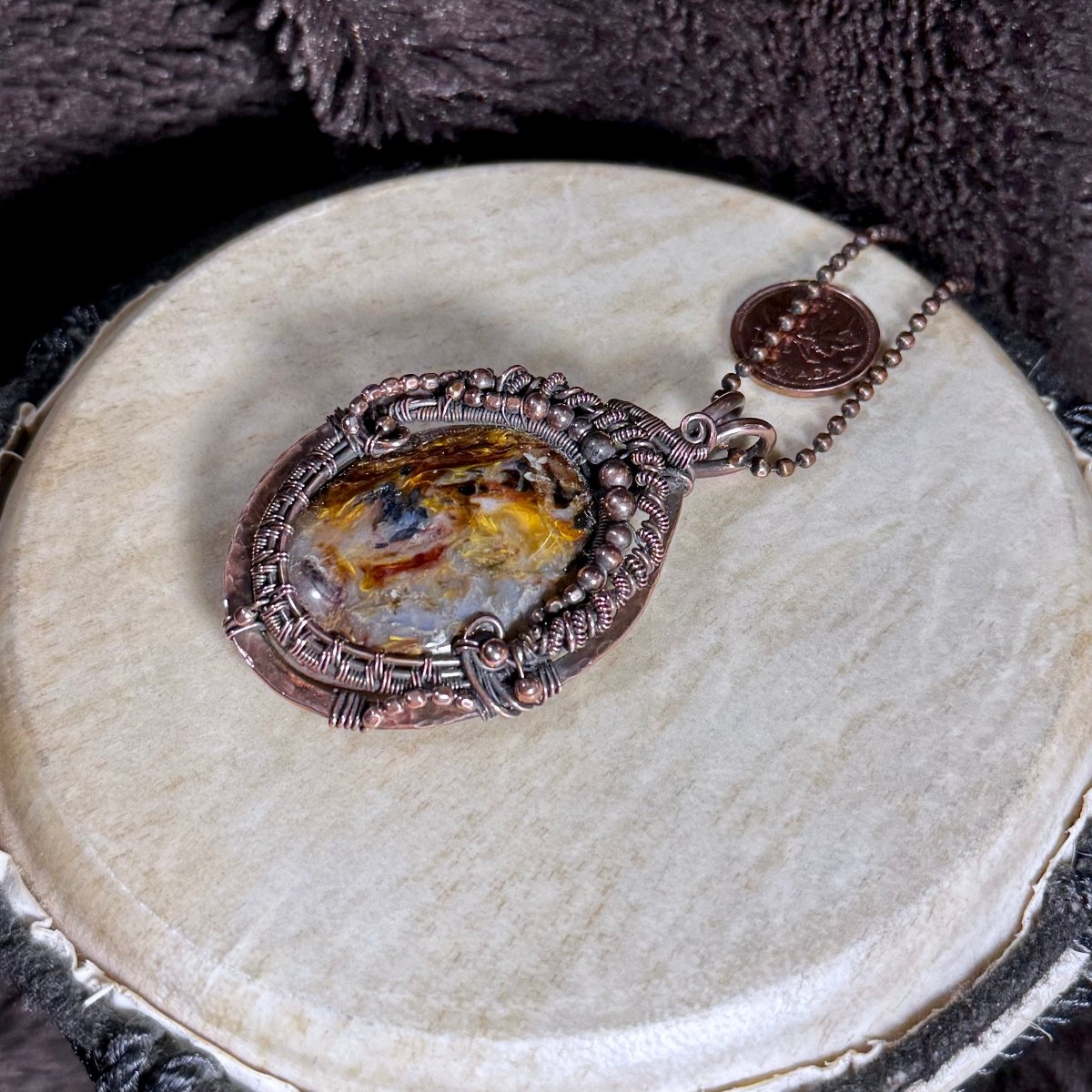 Angled front view of the Pietersite Stormkeeper necklace showing its chatoyant cabochon, antique-inspired copper frame and beaded details.