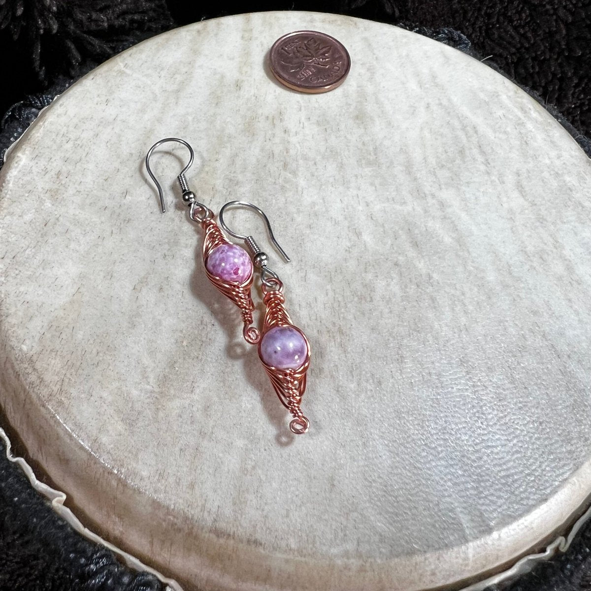 Pair of pink beaded earrings on a round stone surface with a penny for scale.