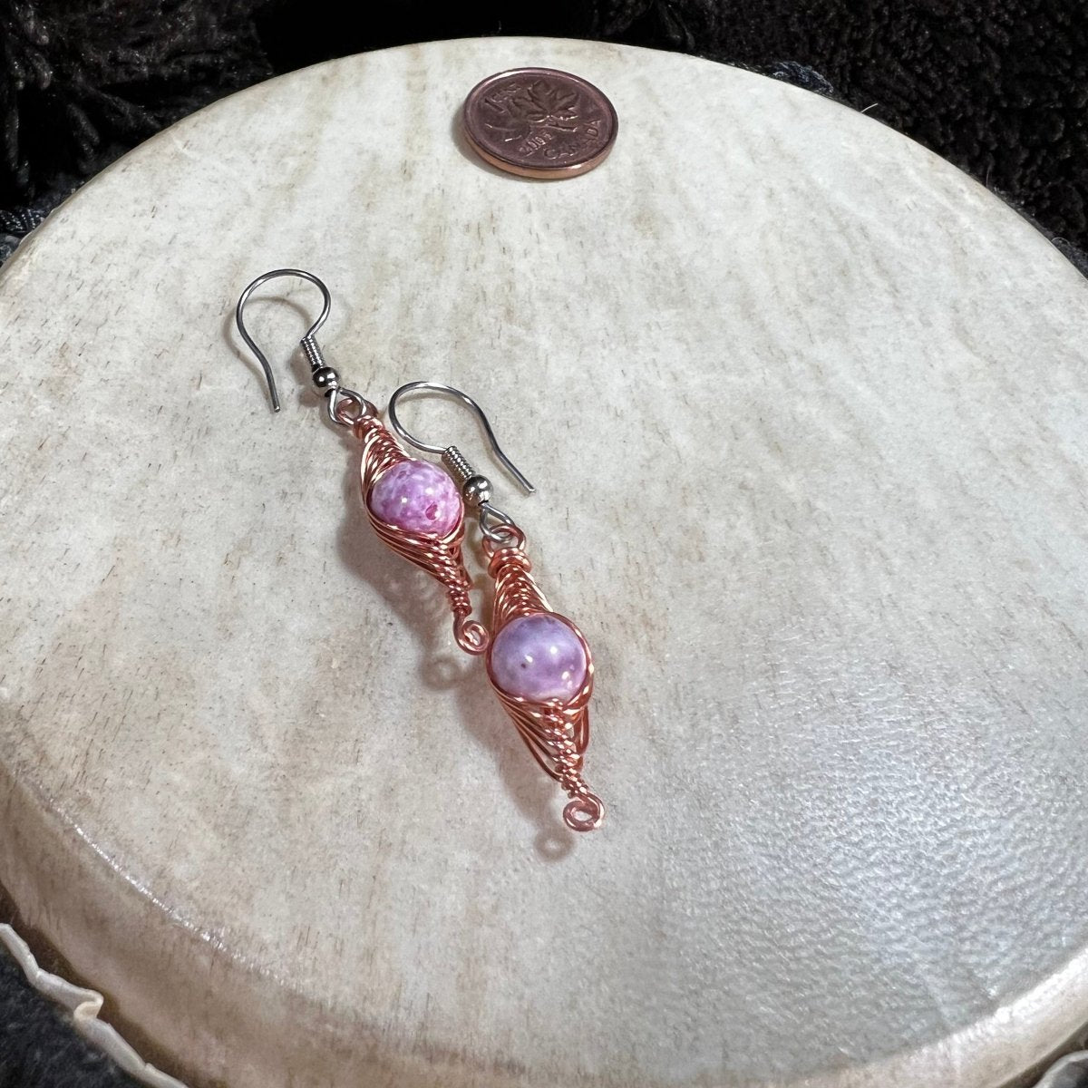 Pair of pink beaded earrings on a round stone surface with a penny for scale.