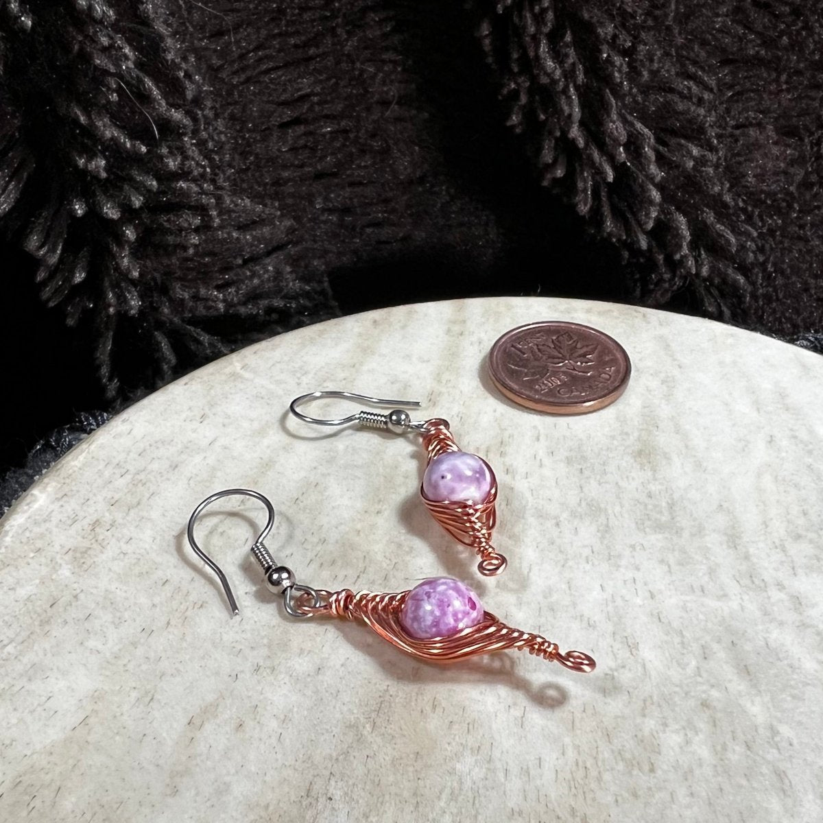 Pair of pink beaded earrings on a round stone surface with a penny for scale.