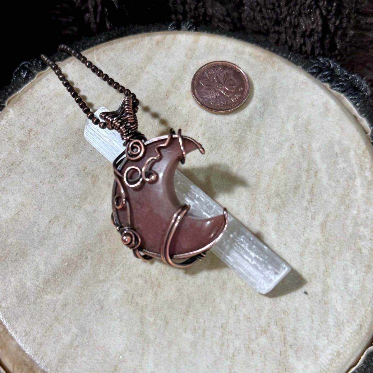 Angled view of the Purple Aventurine Moonwhisper necklace showing its mauve crescent stone, woven copper bail and 21-inch chain.