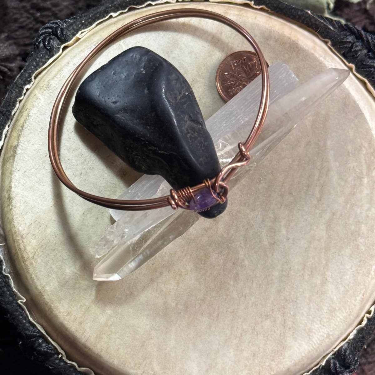 Reclaimed copper and amethyst closed bangle styled over dark stone and white crystal points, with a Canadian penny providing scale.