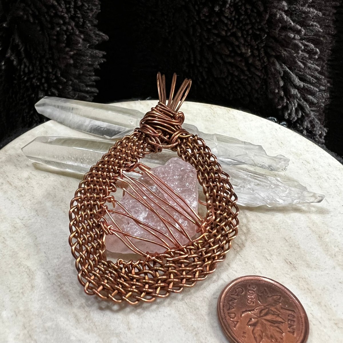 Back view of a raw rose quartz pendant wrapped in handwoven reclaimed copper frame, soft pink natural crystal necklace on neutral background