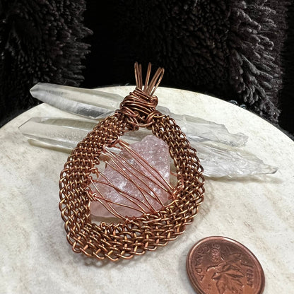 Back view of a raw rose quartz pendant wrapped in handwoven reclaimed copper frame, soft pink natural crystal necklace on neutral background