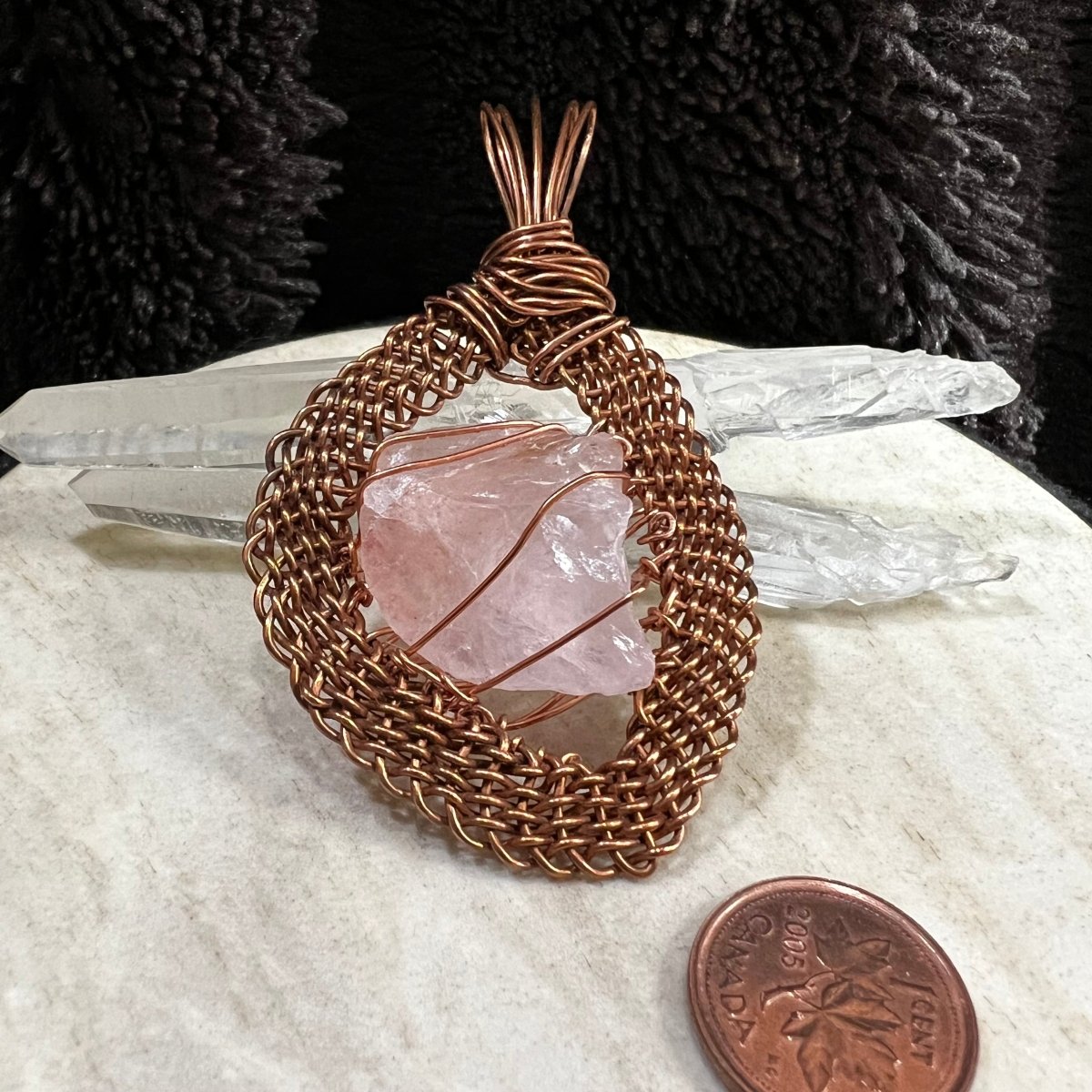 raw rose quartz pendant wrapped in handwoven reclaimed copper frame, soft pink natural crystal necklace on neutral background next to a penny for scale