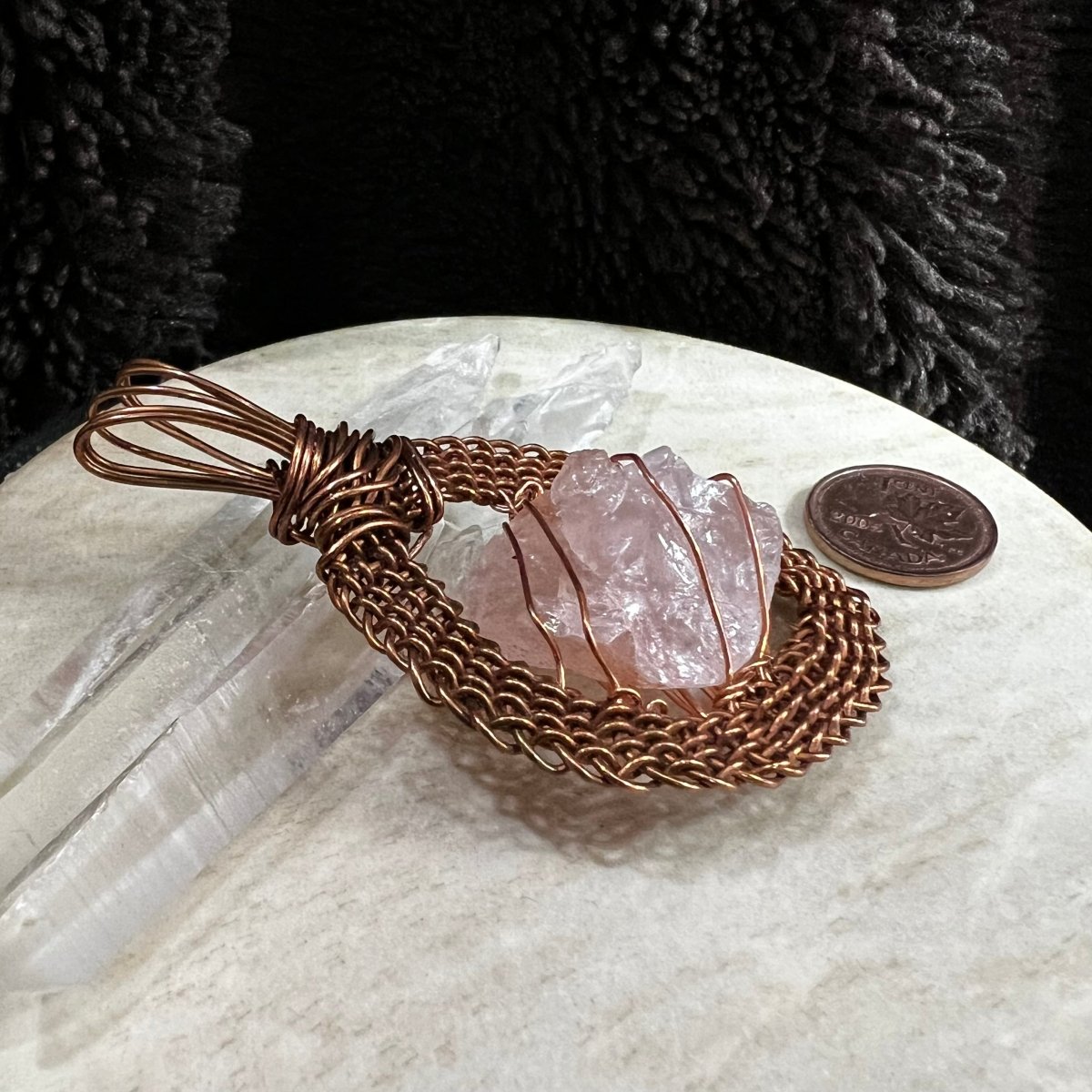 Side view of raw rose quartz pendant wrapped in handwoven reclaimed copper frame, soft pink natural crystal necklace on neutral background