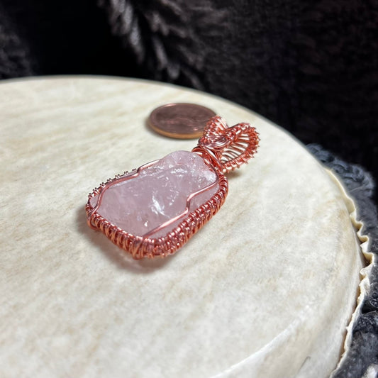 Rose quartz crystal pendant with copper wire wrapping on a textured surface