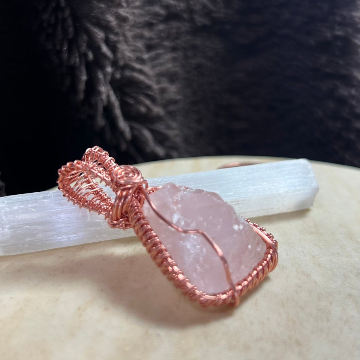 Rose quartz crystal pendant with copper wire wrapping on a textured surface