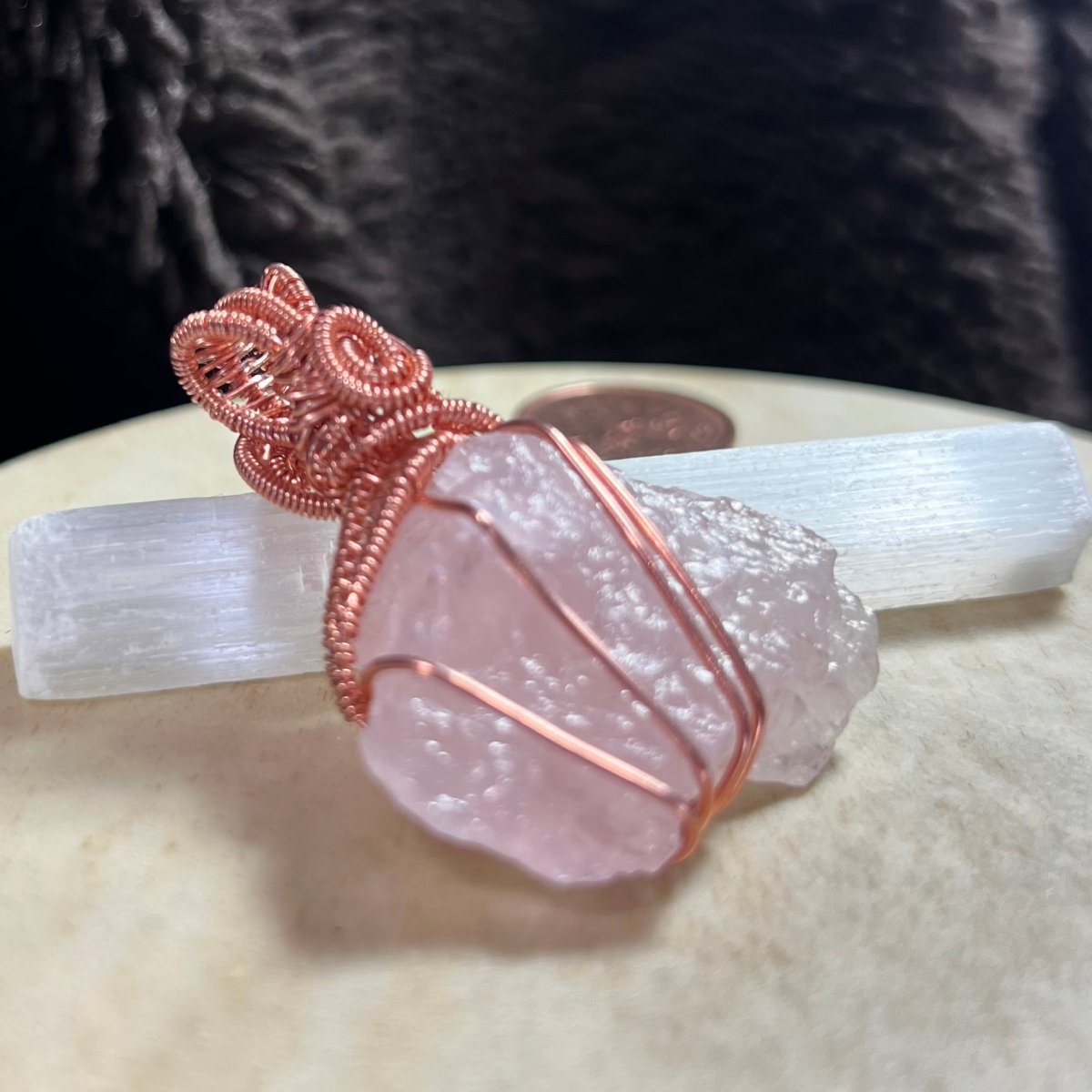 Rose quartz crystal with copper wire wrapping on a white stone