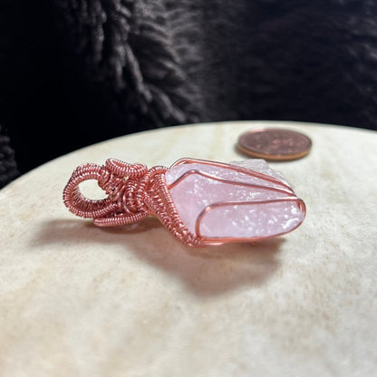 Rose quartz crystal with copper wire wrapping on a white stone
