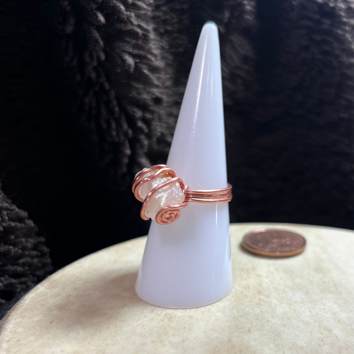 Copper wire wrapped  ring on a white cone-shaped stand with a dark textured background