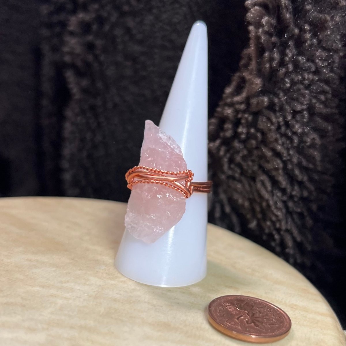 Rose quartz crystal ring with copper wire wrap on a white cone against a dark background