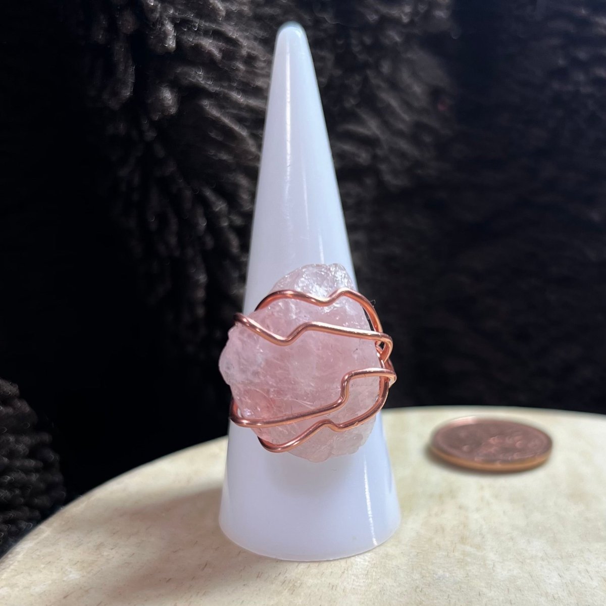 Crystal ring with rose quartz stone on a white cone-shaped object against a dark textured background