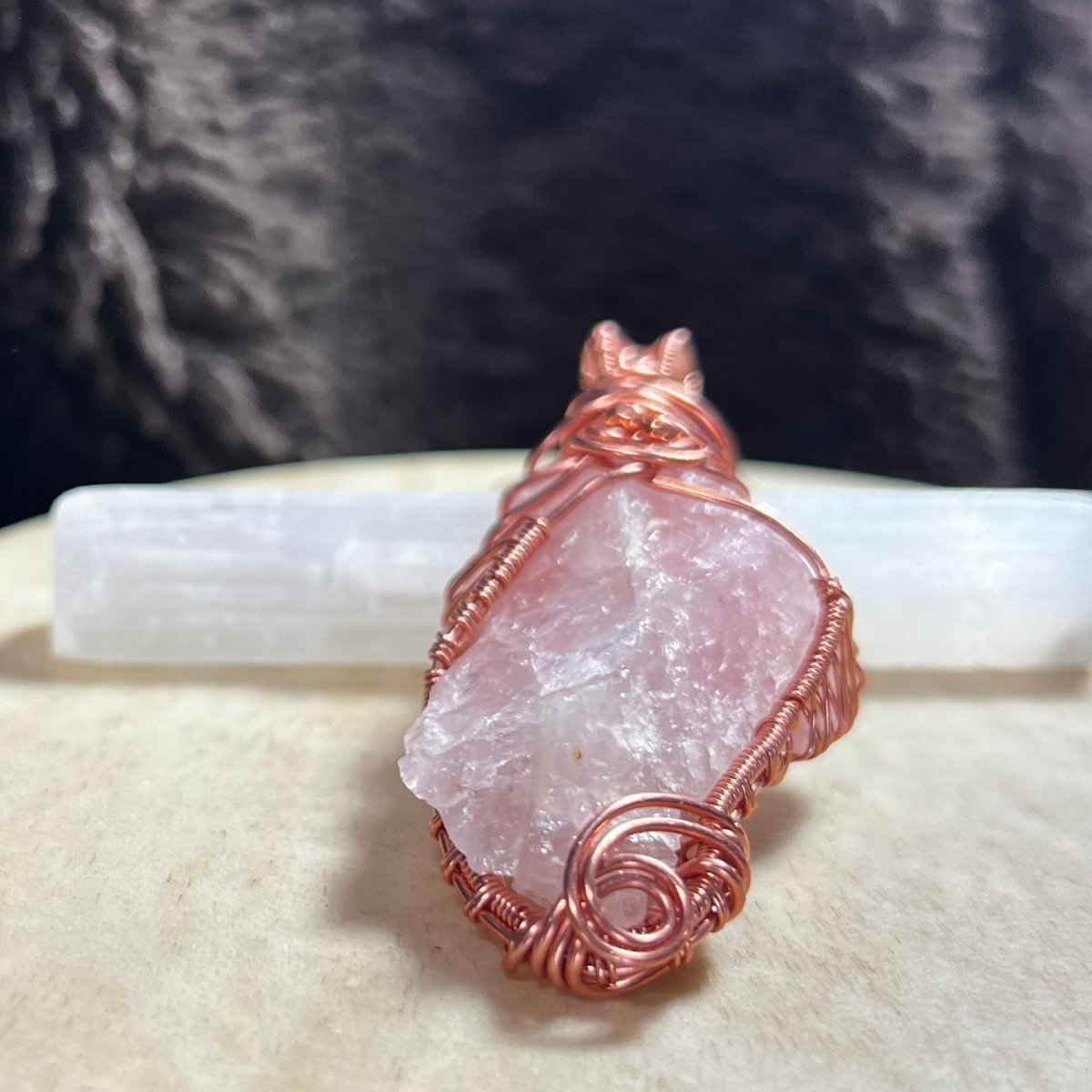 Rose quartz crystal pendant with copper wire wrapping on a textured surface