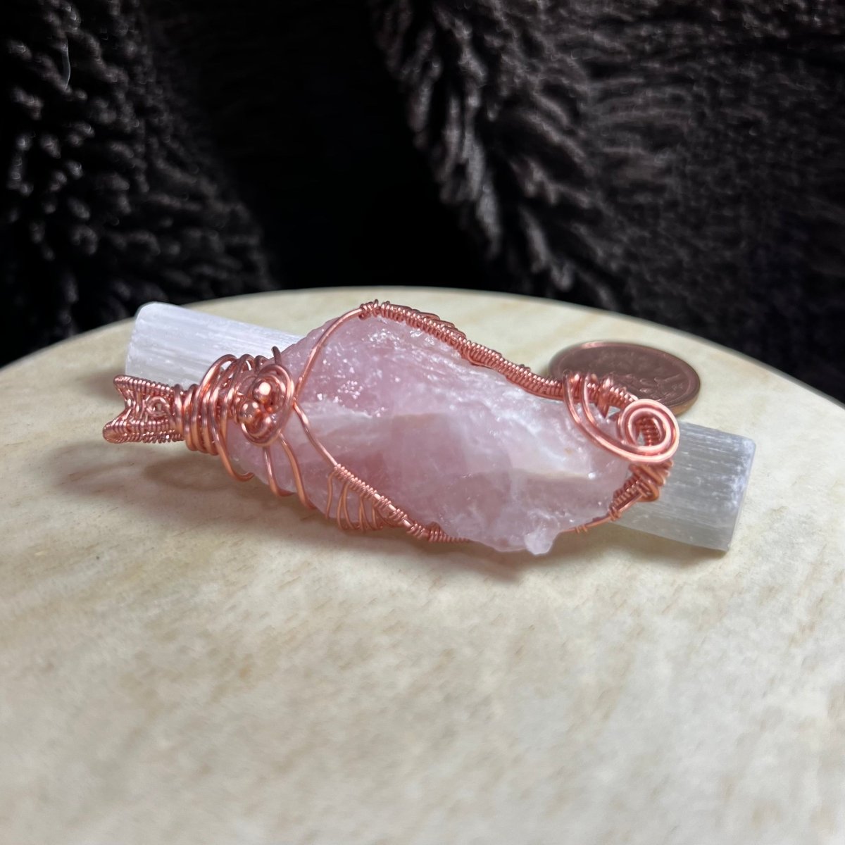 Rose quartz crystal pendant with copper wire wrapping on a textured surface