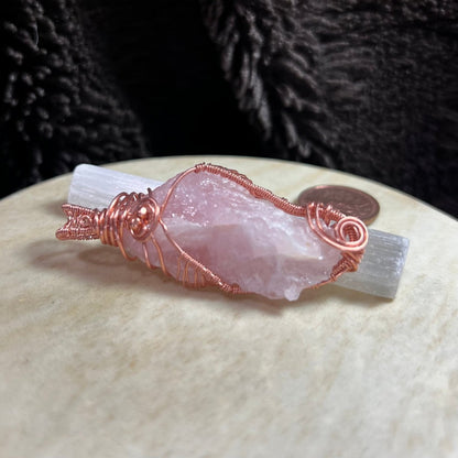 Rose quartz crystal pendant with copper wire wrapping on a textured surface