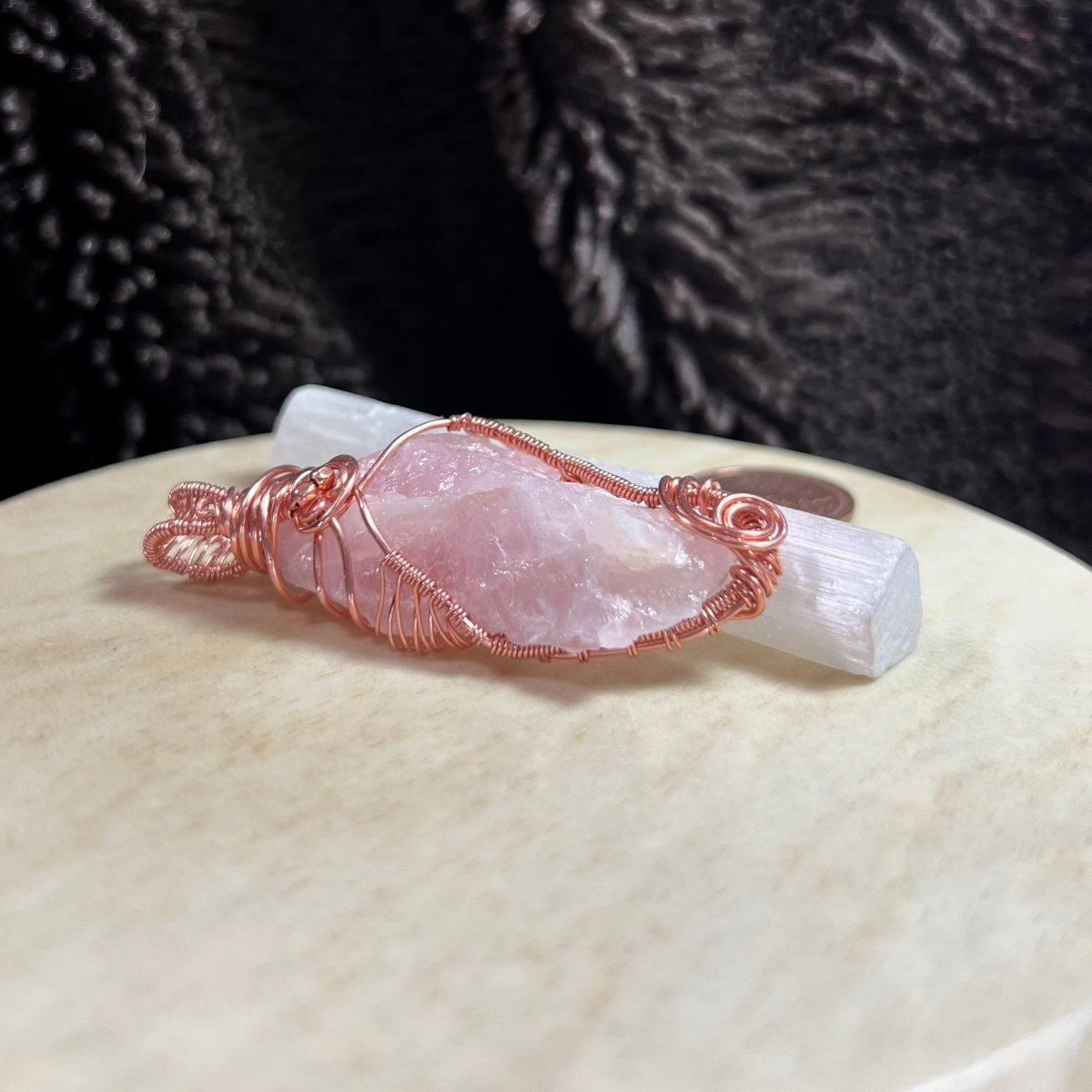 Rose quartz crystal pendant with copper wire wrapping on a textured surface