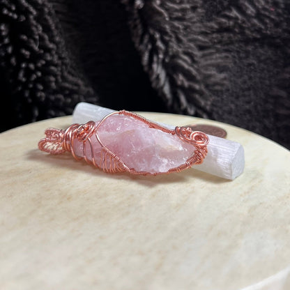 Rose quartz crystal pendant with copper wire wrapping on a textured surface