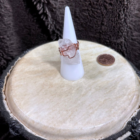 Front view of a raw pale pink rose quartz crystal wrapped in reclaimed copper as a handmade size 6 spiral ring.