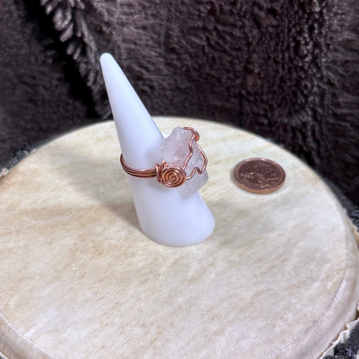 Detailed angled view of a raw rose quartz crystal secured in flowing reclaimed copper with a symbolic spiral accent.