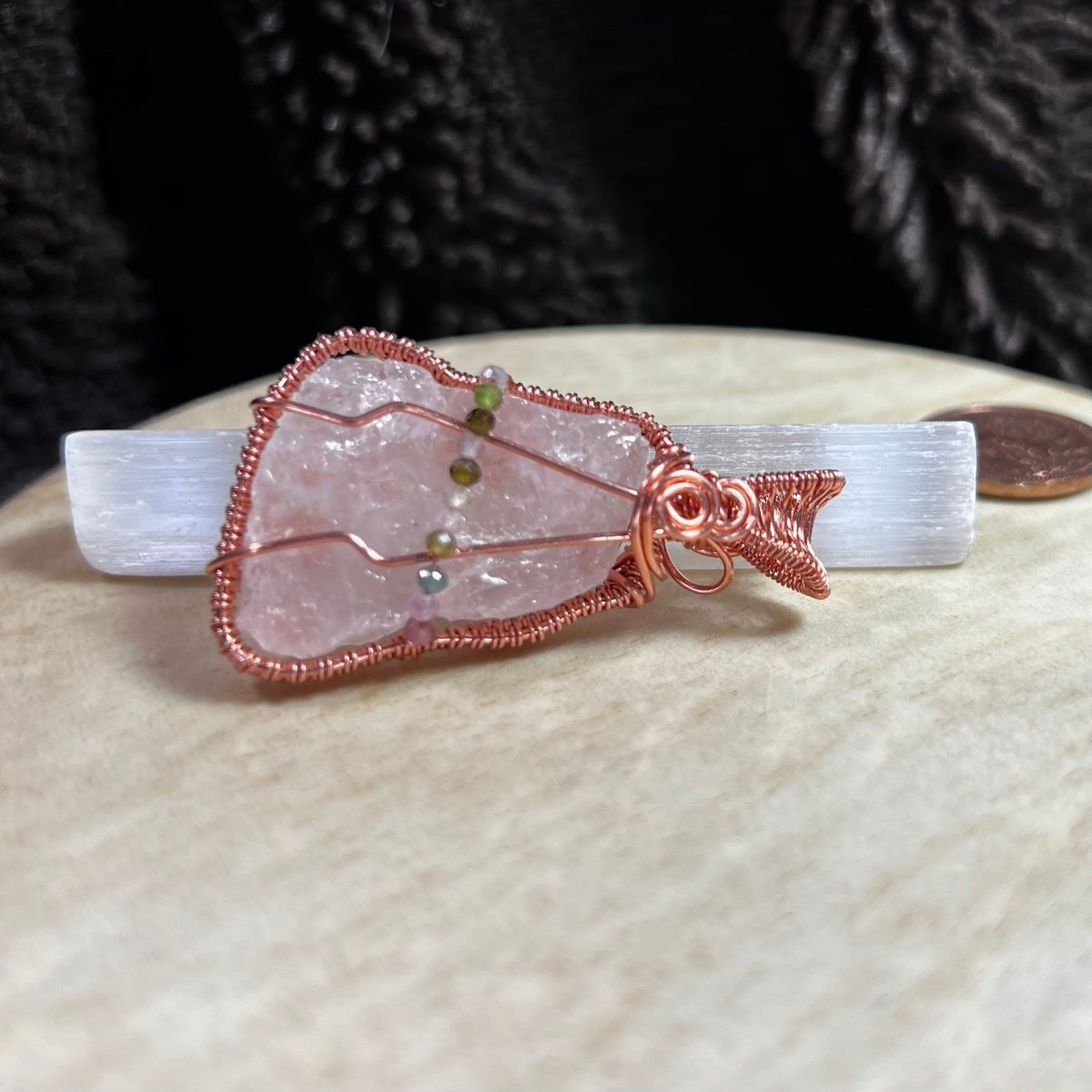 Raw rose quartz crystal pendant with copper wire wrapping on a beige surface