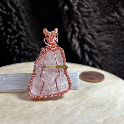 Raw rose quartz crystal pendant with copper wire wrapping on a beige surface