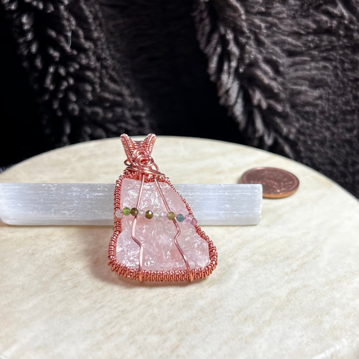 Raw rose quartz crystal pendant with copper wire wrapping on a beige surface