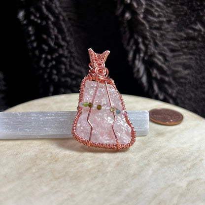 Raw rose quartz crystal pendant with copper wire wrapping on a beige surface