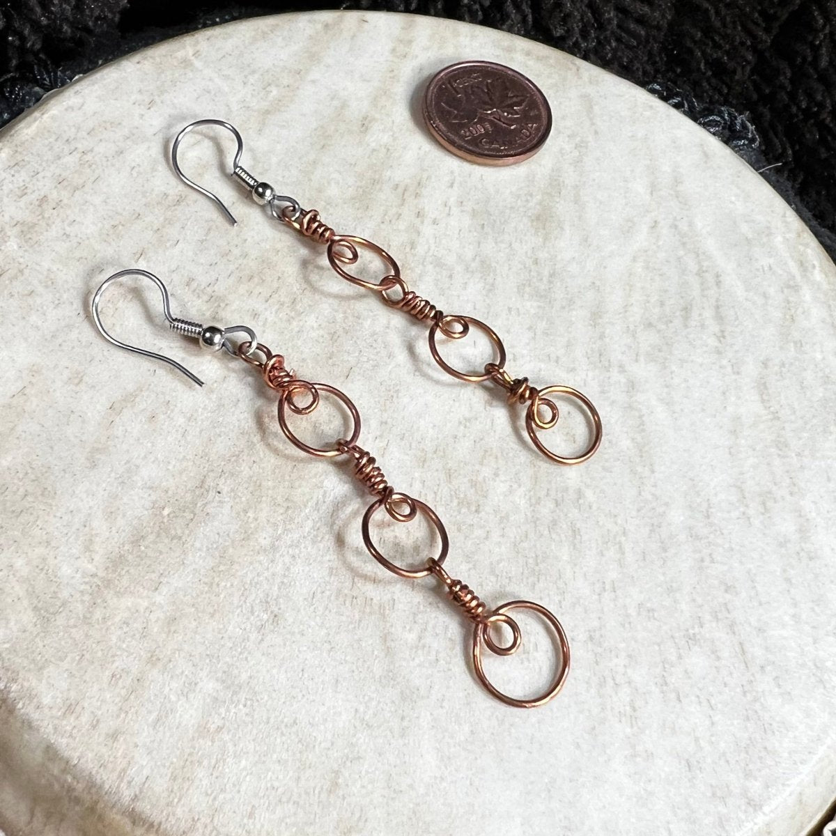Handmade copper wire spiral chain earrings with circular links and surgical steel ear wires, photographed with Canadian penny for scale.